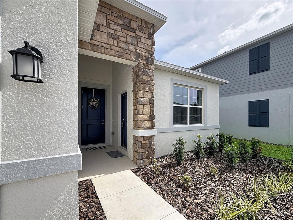 The exterior of a house features a stone-accented entryway, a dark front door, and landscaping — 3660 ROLLING RIDGE BEND, DAVENPORT, FL