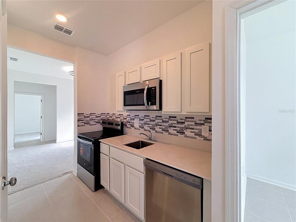 A small kitchen features white cabinets, stainless steel appliances, and a tiled backsplash — 3660 ROLLING RIDGE BEND, DAVENPORT, FL