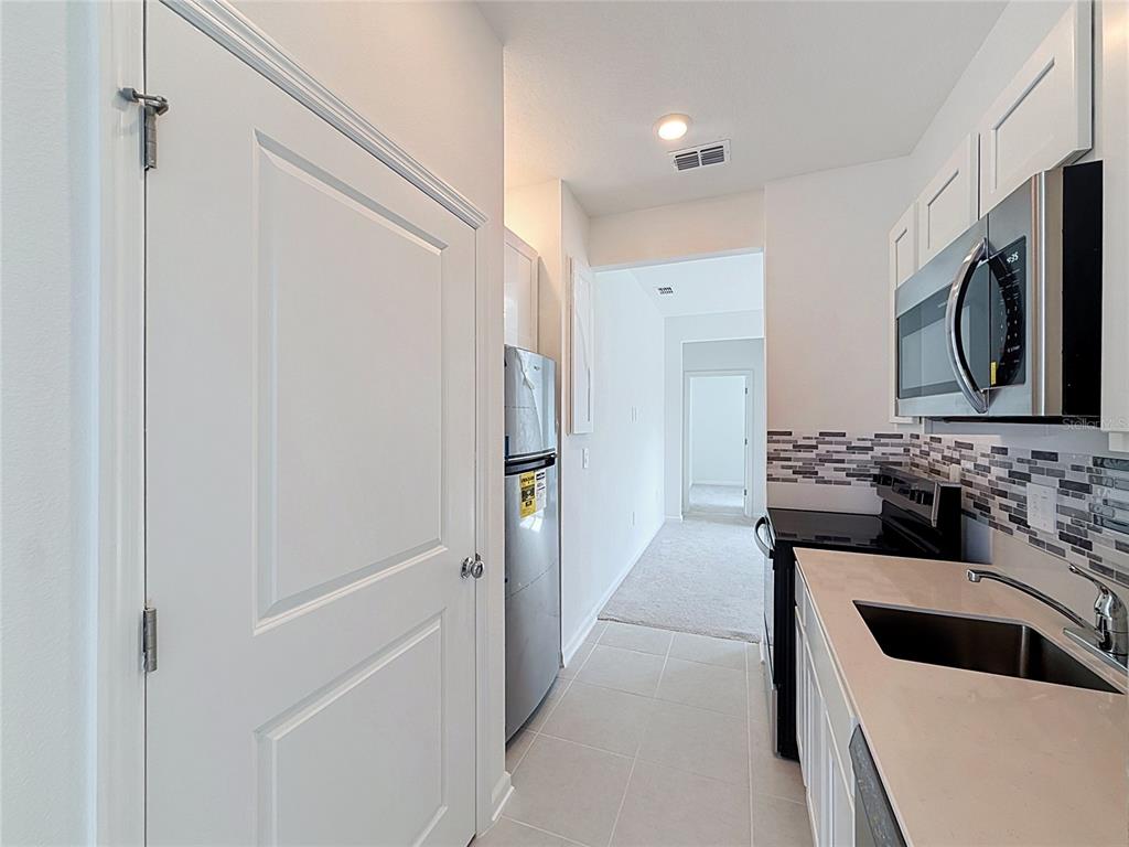A kitchen with white cabinets, stainless steel appliances, and a tiled backsplash leads to a hallway — 3660 ROLLING RIDGE BEND, DAVENPORT, FL