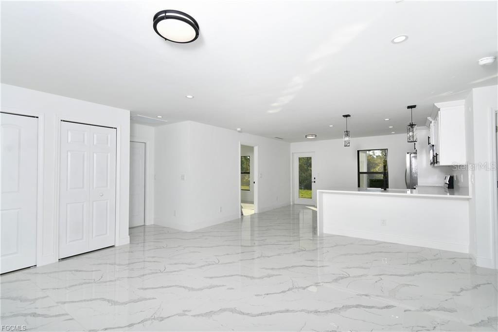 A bright, open-concept kitchen and living area features white cabinetry and polished marble-patterned tile floors — 3417 57TH STREET W, LEHIGH ACRES, FL