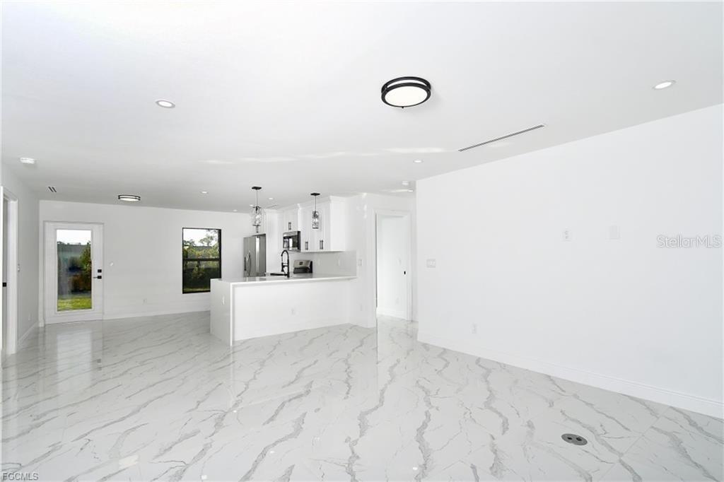 A bright, open-concept kitchen and living area features white cabinetry, marble-patterned tile flooring, and recessed lighting — 3417 57TH STREET W, LEHIGH ACRES, FL