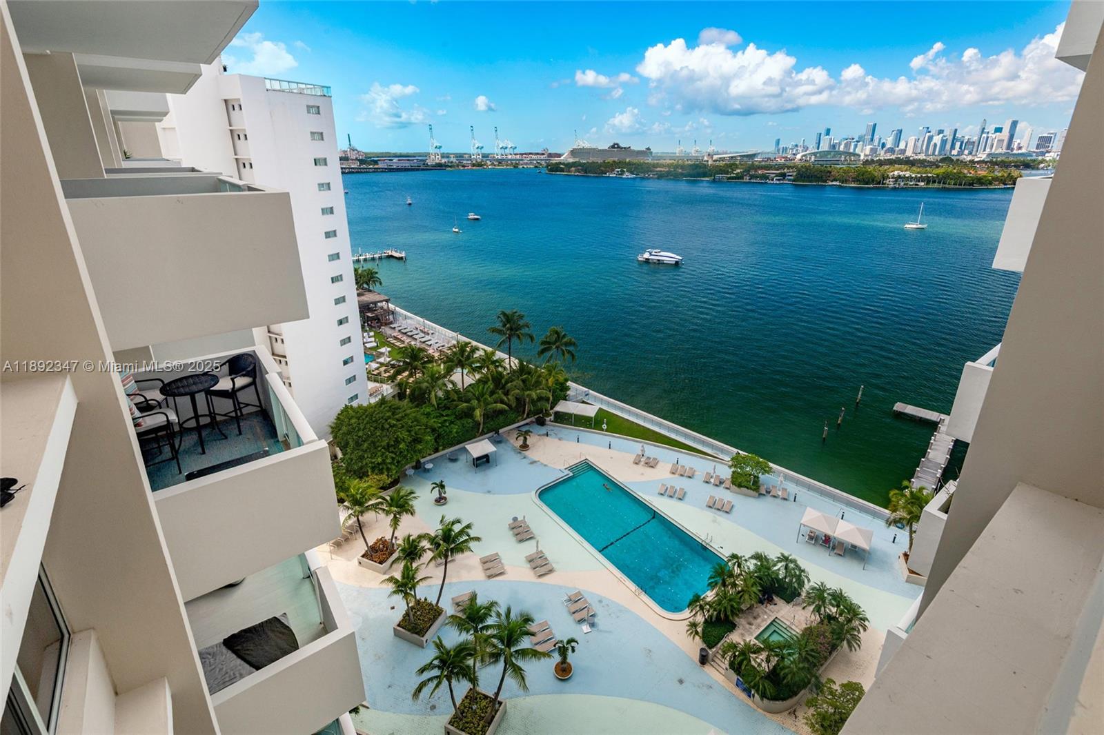 An elevated view shows a building balcony overlooking a swimming pool, palm trees, and bay — 1200 West Ave # 1531, Miami Beach FL 33139, MIAMI BEACH, FL