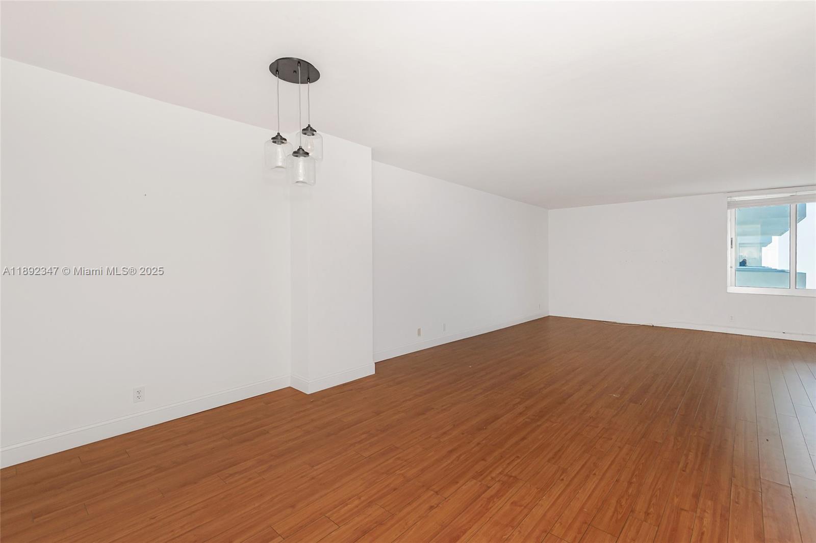 An empty room features white walls, wood-look flooring, a three-light pendant fixture, and a window — 1200 West Ave # 1531, Miami Beach FL 33139, MIAMI BEACH, FL