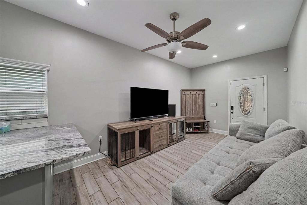 A living room features a grey sofa, a wooden media console with dog crates, and tile flooring — 2341 W CHESTNUT STREET, TAMPA, FL