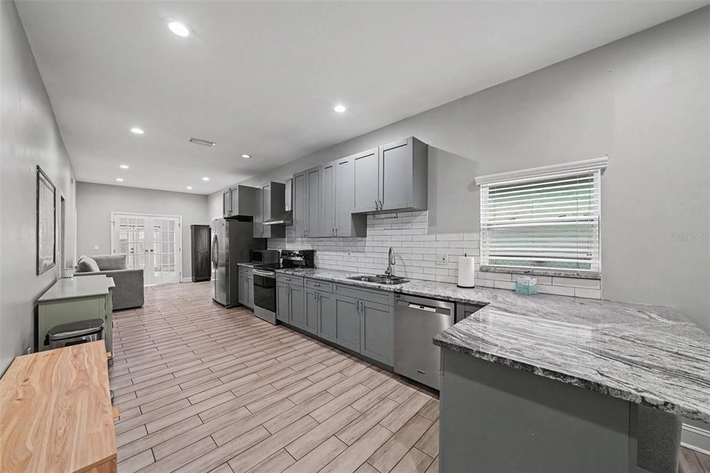 A kitchen features gray cabinets, granite countertops, stainless steel appliances, and light wood-look tile flooring — 2341 W CHESTNUT STREET, TAMPA, FL