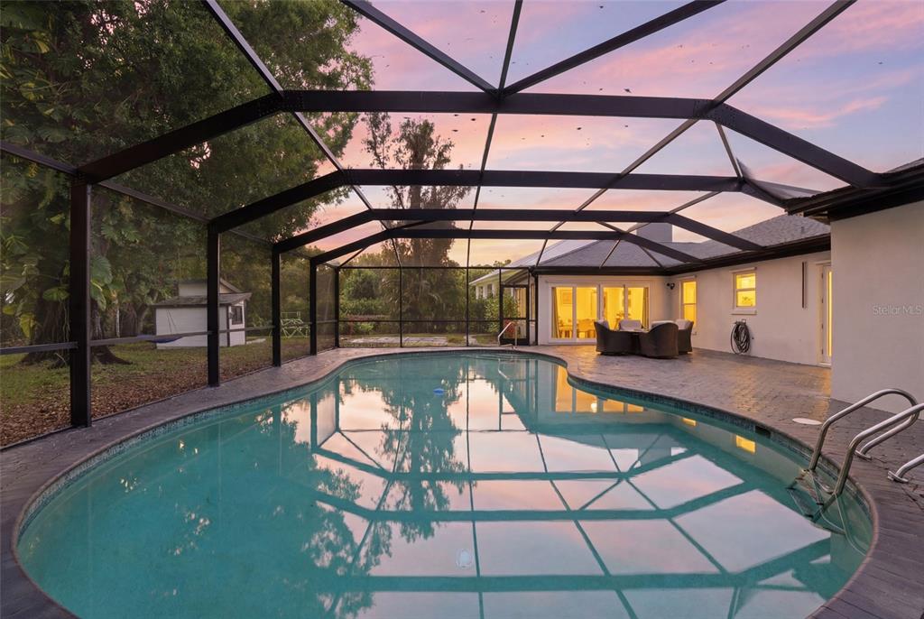 A screened-in swimming pool and patio area at sunset with a house in the background — 3931 W RIVERSIDE DRIVE, FORT MYERS, FL