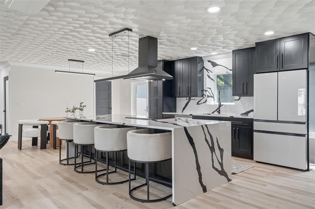 A modern kitchen features black cabinetry, a waterfall quartz island, and a textured white ceiling — 3931 W RIVERSIDE DRIVE, FORT MYERS, FL