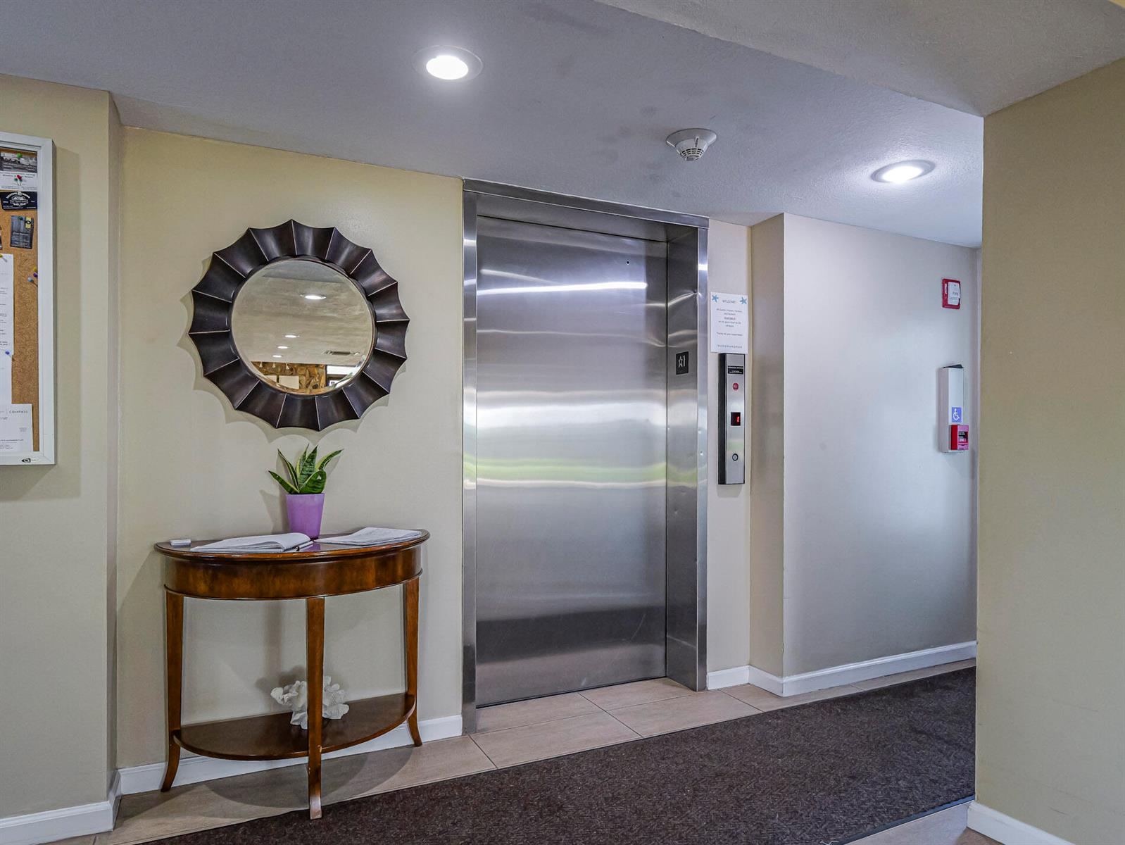 An elevator with stainless steel doors sits next to a console table and round mirror — 4141 Ocean Drive # 403, Vero Beach FL 32963, VERO BEACH, FL