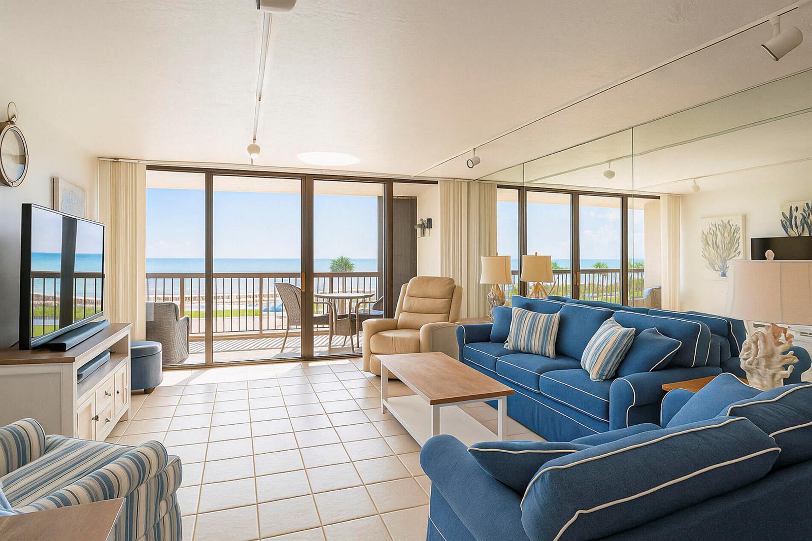 A living room with blue sofas, tile flooring, and a balcony overlooking the ocean — 4141 Ocean Drive # 403, Vero Beach FL 32963, VERO BEACH, FL