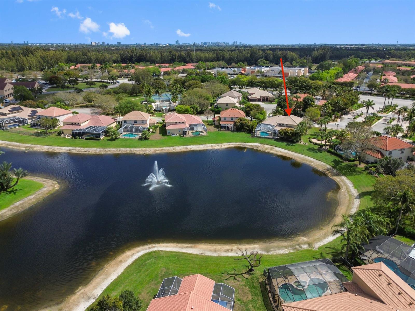 An aerial view shows a residential neighborhood with houses surrounding a lake with a fountain — 3638 Hamilton Key, West Palm Beach FL 33411, WEST PALM BEACH, FL