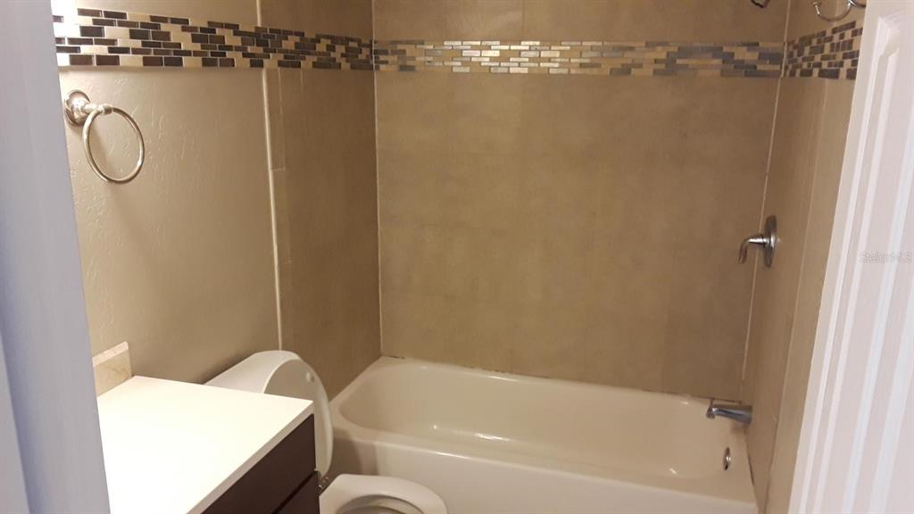 A bathroom features a white bathtub, a toilet, and a vanity with a tiled wall — 200 COUNTRY CLUB DRIVE UNIT 801, LARGO, FL