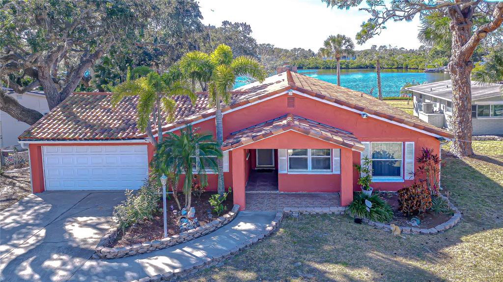 A single-story, terracotta-colored house with a tiled roof sits near a body of water — 7051 MORNINGSTAR LANE, NEW PORT RICHEY, FL