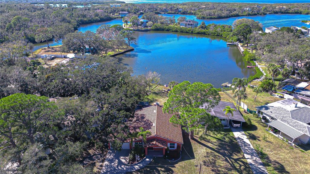 An aerial view shows a house with a brown roof situated near a large lake — 7051 MORNINGSTAR LANE, NEW PORT RICHEY, FL