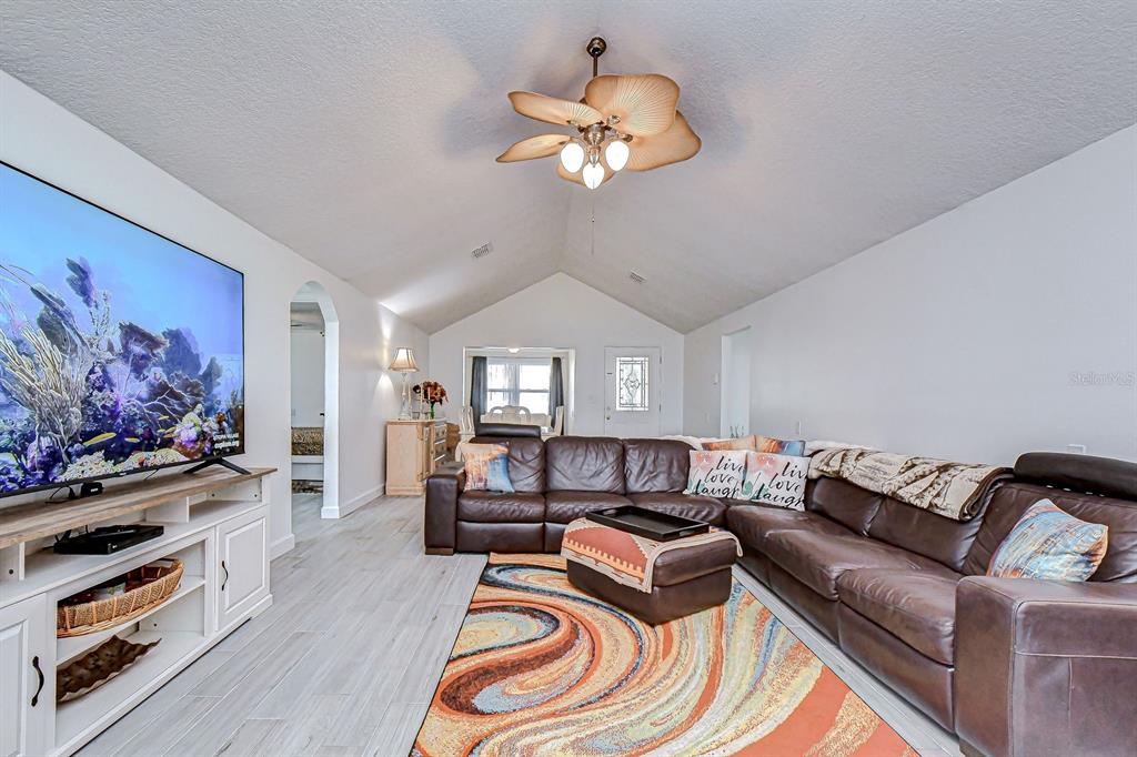 A living room features a vaulted ceiling, brown leather sectional, and a colorful area rug — 7051 MORNINGSTAR LANE, NEW PORT RICHEY, FL