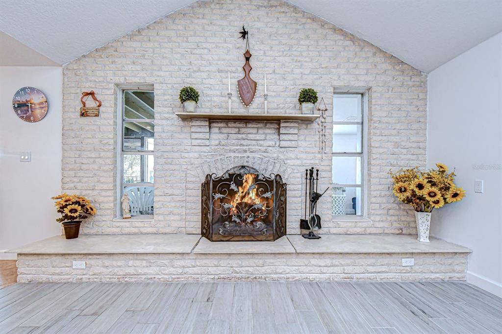 A living room features a white brick fireplace with a hearth and two flanking windows — 7051 MORNINGSTAR LANE, NEW PORT RICHEY, FL