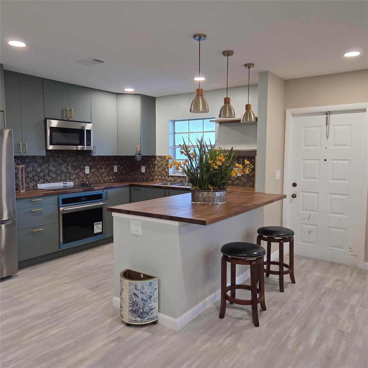 A kitchen features green cabinets, wood countertops, a central island with bar stools, and pendant lighting — 5385 Lakefront Boulevard # A, Delray Beach FL 33484, DELRAY BEACH, FL