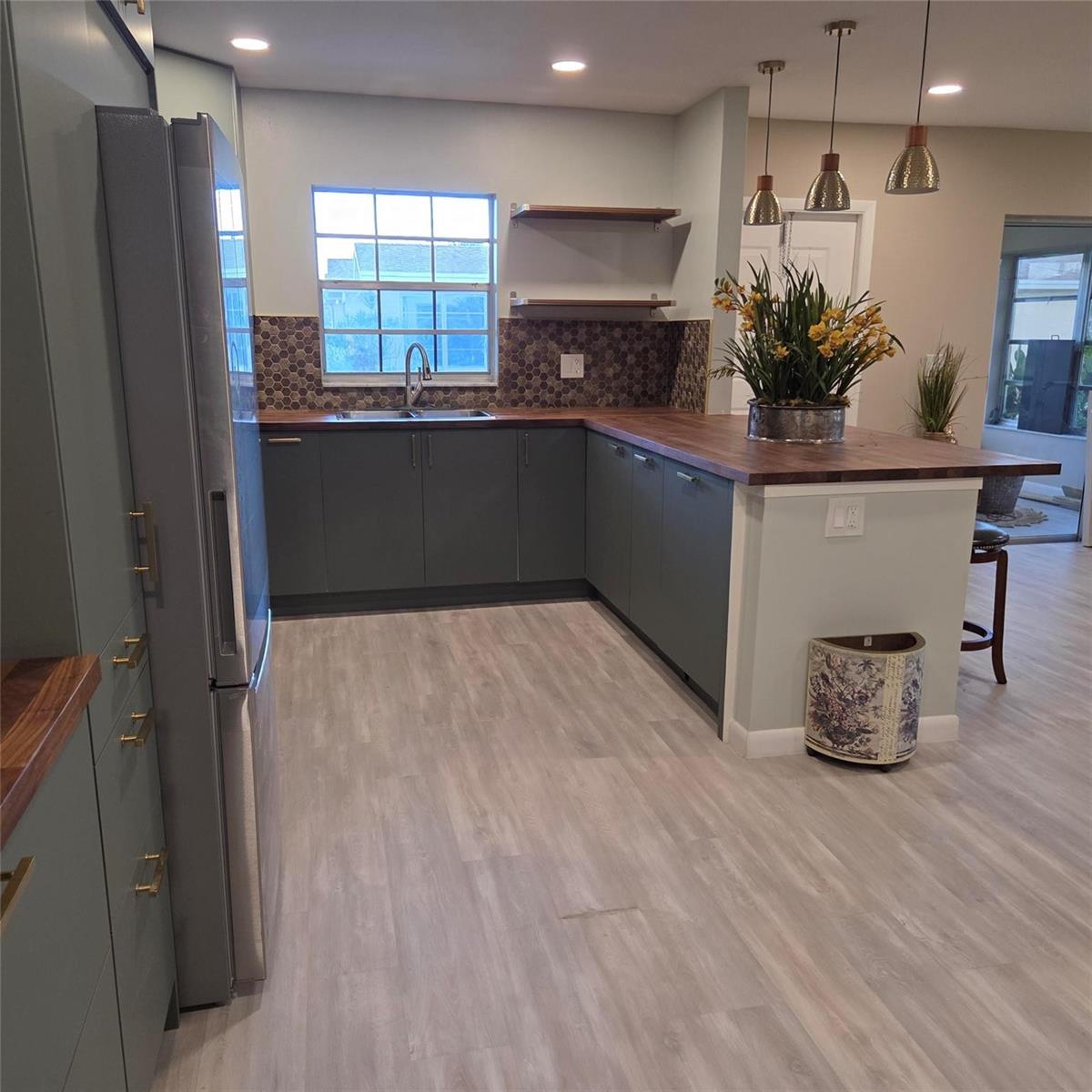 A kitchen features dark green cabinets, wood countertops, a hexagonal tile backsplash, and light flooring — 5385 Lakefront Boulevard # A, Delray Beach FL 33484, DELRAY BEACH, FL