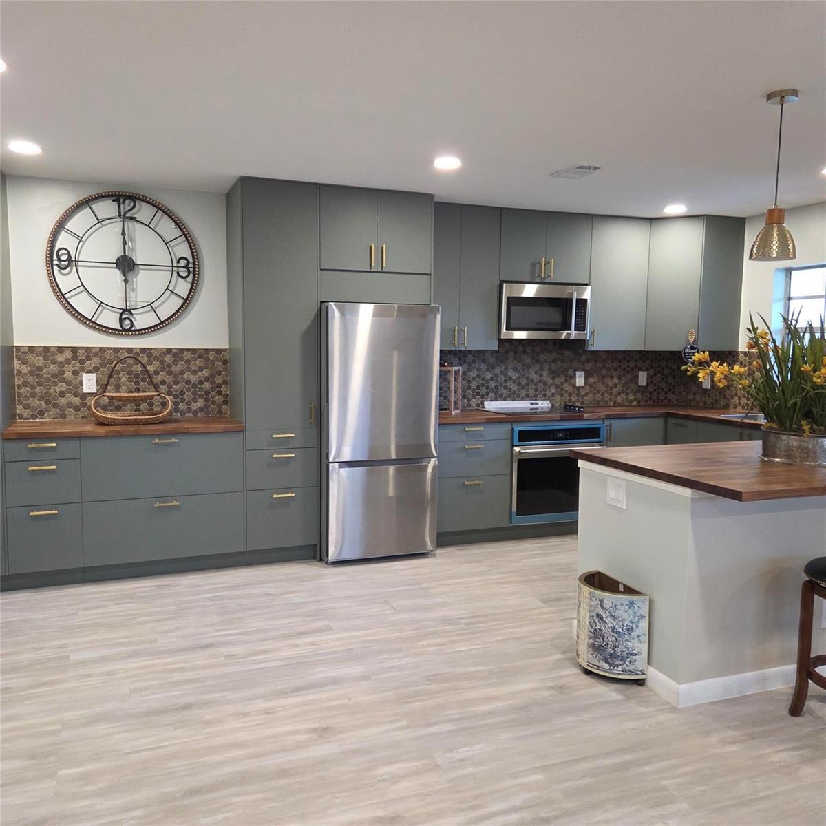 A kitchen features sage green cabinets, wood countertops, a honeycomb backsplash, and stainless steel appliances — 5385 Lakefront Boulevard # A, Delray Beach FL 33484, DELRAY BEACH, FL