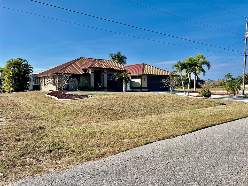 A single-story house with a metal roof and palm trees sits on a grassy lot — 426 NW 37TH PLACE, CAPE CORAL, FL