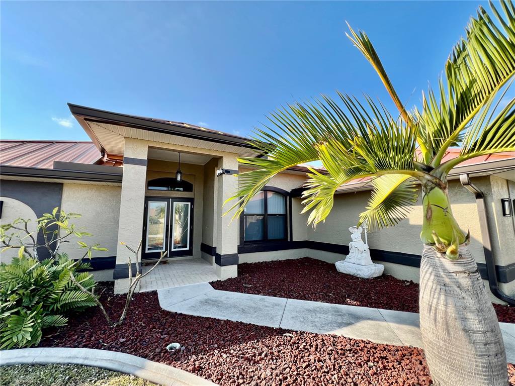 The exterior of a stucco home features a covered entryway, a palm tree, and landscaping — 426 NW 37TH PLACE, CAPE CORAL, FL