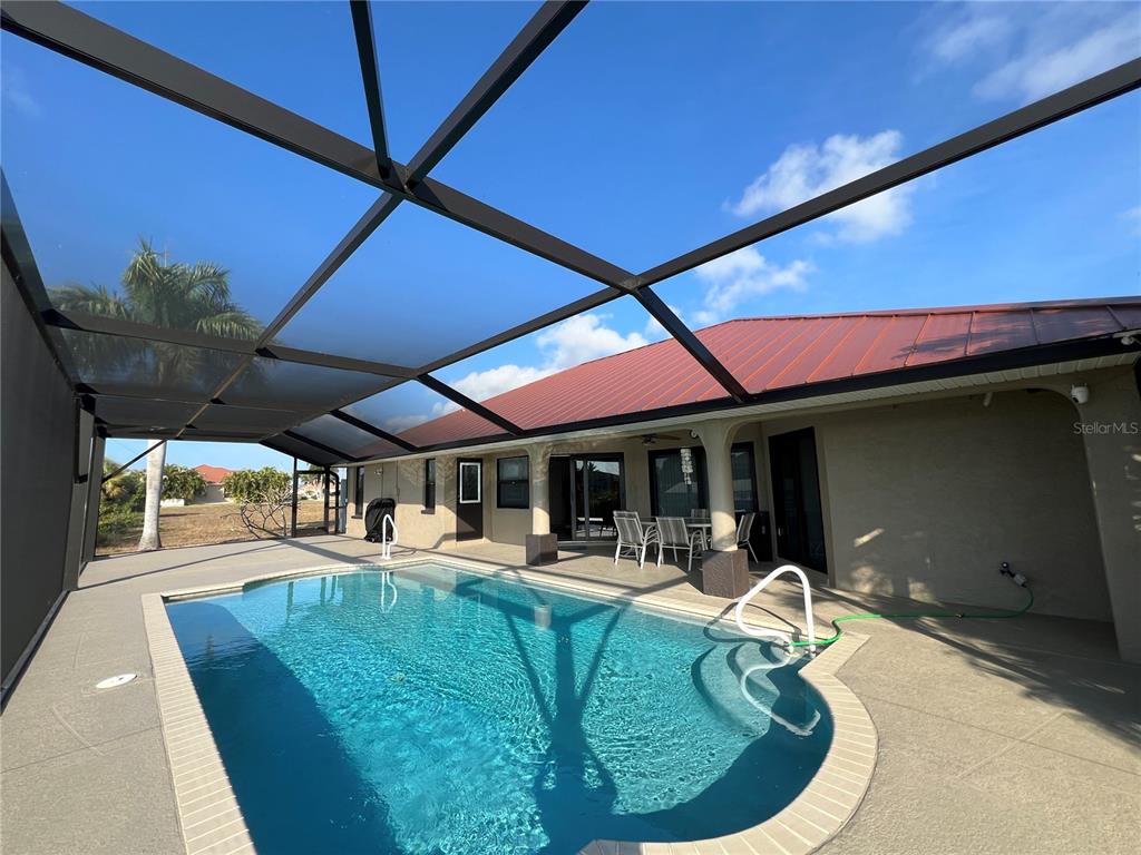 A swimming pool sits inside a screened-in lanai attached to a house with a metal roof — 426 NW 37TH PLACE, CAPE CORAL, FL