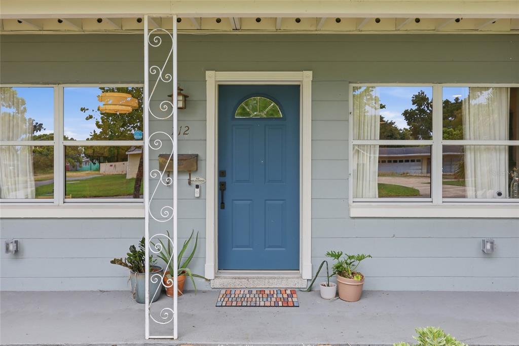 A blue front door is centered on the light gray exterior wall of a house — 712 MALONE DRIVE, ORLANDO, FL