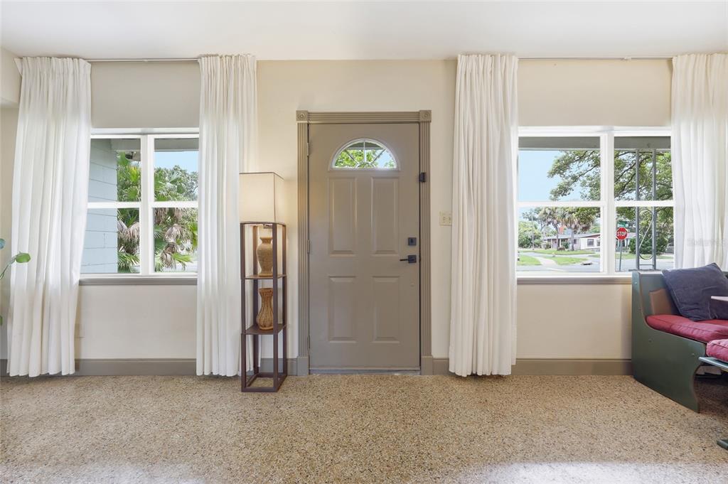 A living room with carpeted floors, two windows with white curtains, and a central front door — 712 MALONE DRIVE, ORLANDO, FL