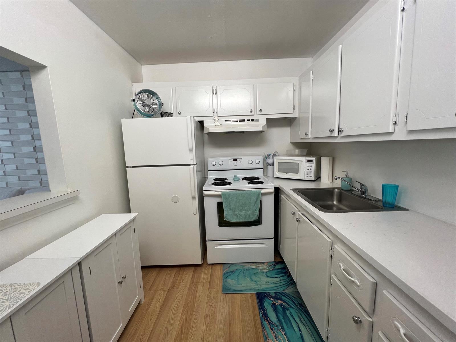 A small kitchen features white cabinets, white appliances, a stainless steel sink, and wood flooring — 258 Markham L # 258, Deerfield Beach FL 33442, DEERFIELD BEACH, FL