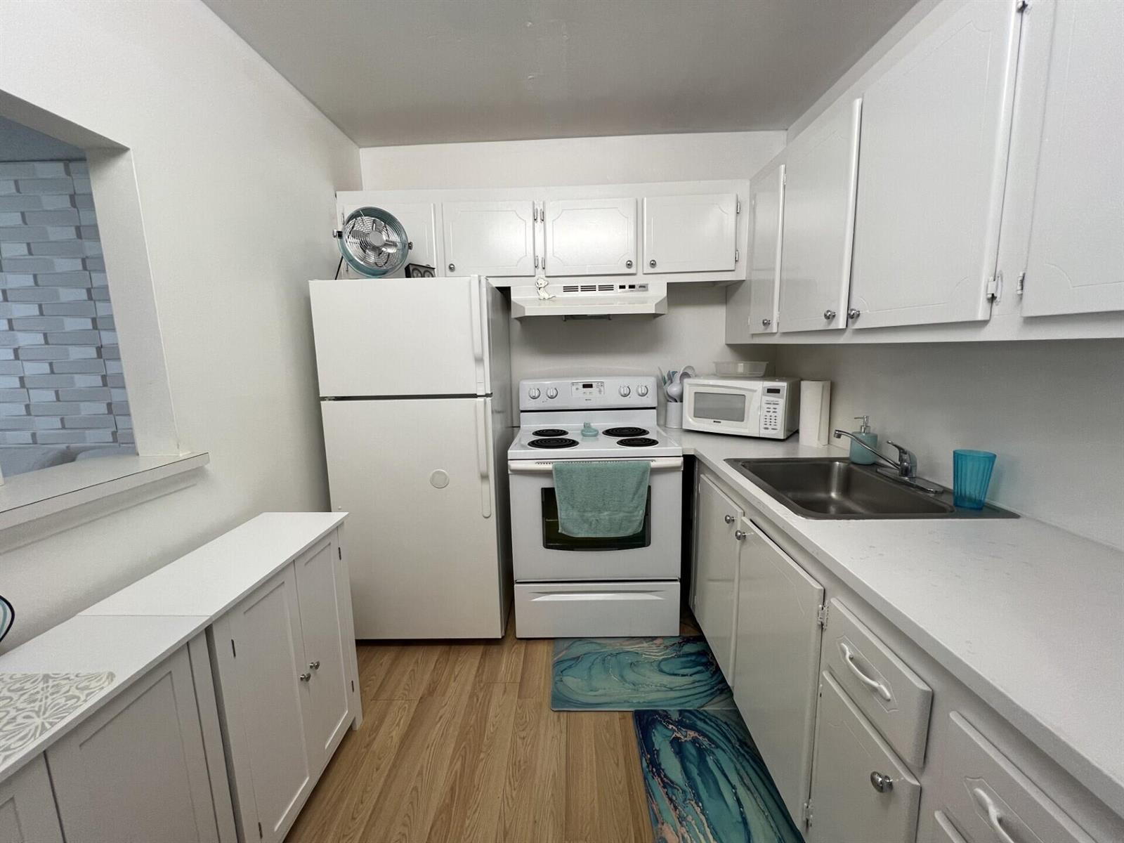 A small kitchen features white cabinets, white appliances, a stainless steel sink, and wood flooring — 258 Markham L # 258, Deerfield Beach FL 33442, DEERFIELD BEACH, FL