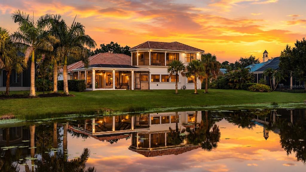A two-story house with a screened-in patio sits beside a pond at sunset — 3548 FOUNDERS CLUB DRIVE, SARASOTA, FL