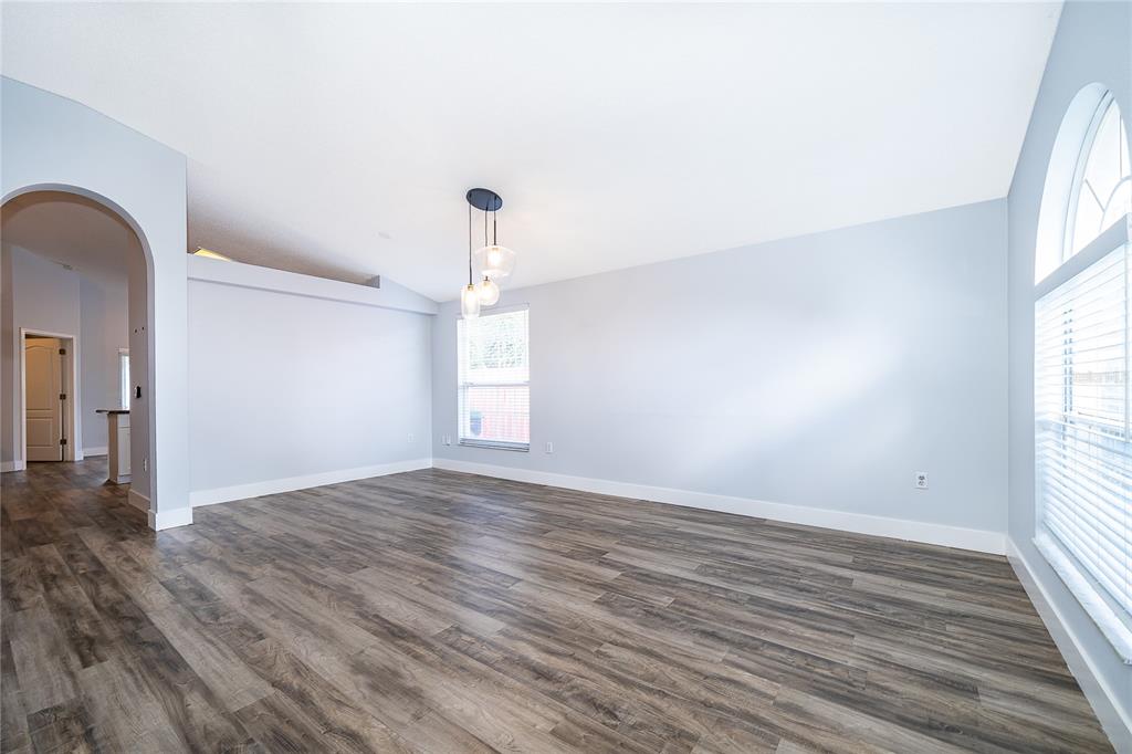 An empty room with light blue walls, wood-look flooring, a modern pendant light, and arched windows — 13233 HEMING WAY, ORLANDO, FL