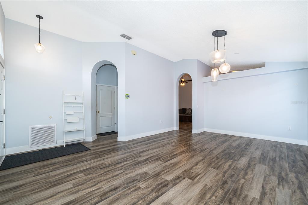 An empty room with light blue walls, wood-look flooring, arched doorways, and modern pendant lighting — 13233 HEMING WAY, ORLANDO, FL