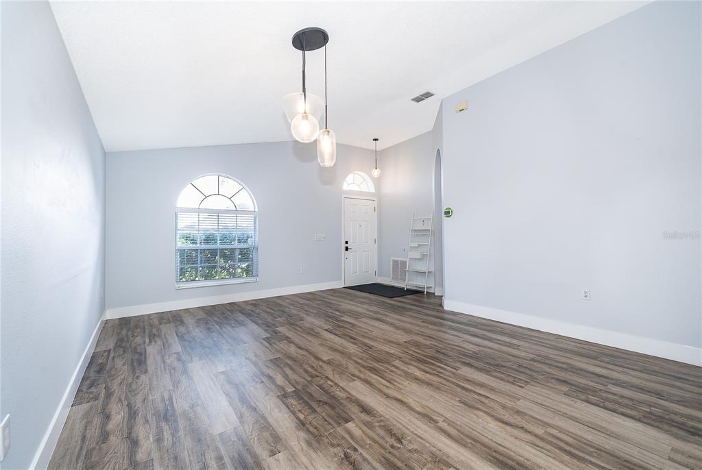An empty room features light blue walls, wood-look flooring, and a modern three-pendant light fixture — 13233 HEMING WAY, ORLANDO, FL