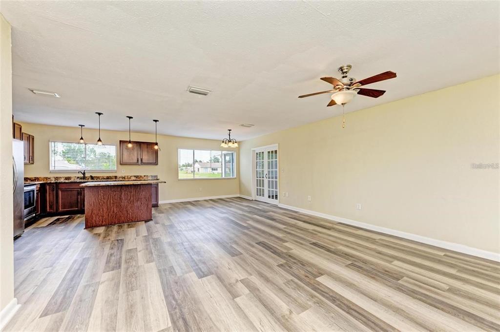 An open-concept kitchen and living area featuring wood-look flooring, dark cabinets, and a ceiling fan — 7120 ELYTON DRIVE, NORTH PORT, FL