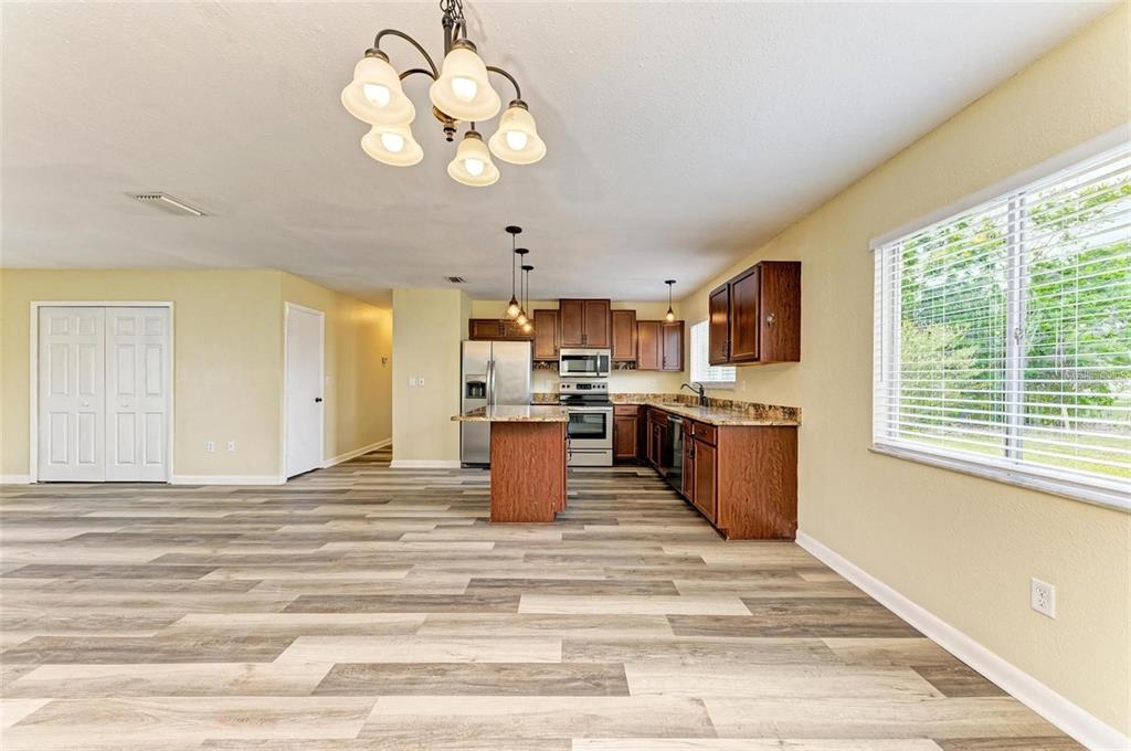 A kitchen with wood cabinets, granite countertops, and a center island opens to a room — 7120 ELYTON DRIVE, NORTH PORT, FL