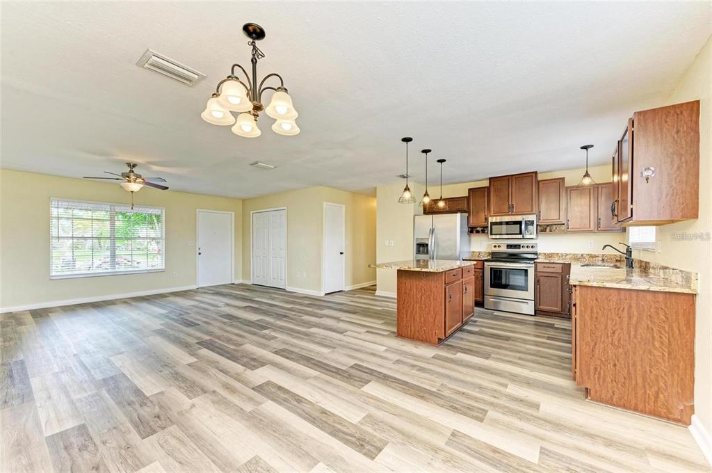 An open-concept kitchen and living area featuring wood-look flooring, wood cabinets, and granite countertops — 7120 ELYTON DRIVE, NORTH PORT, FL