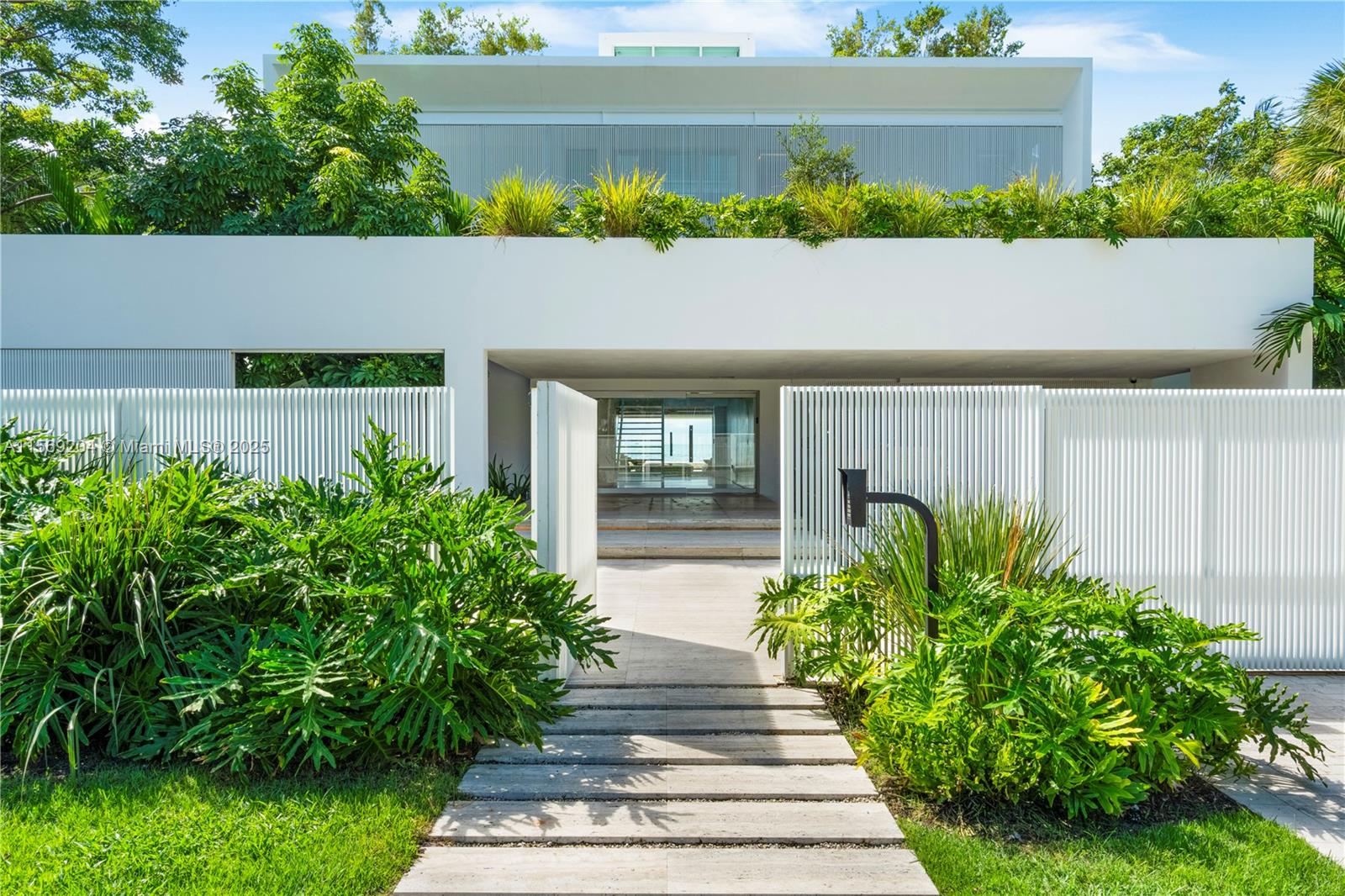 A modern white house features a slatted fence, a stone walkway, and lush tropical landscaping — 440 S Mashta Dr, Key Biscayne FL 33149, KEY BISCAYNE, FL