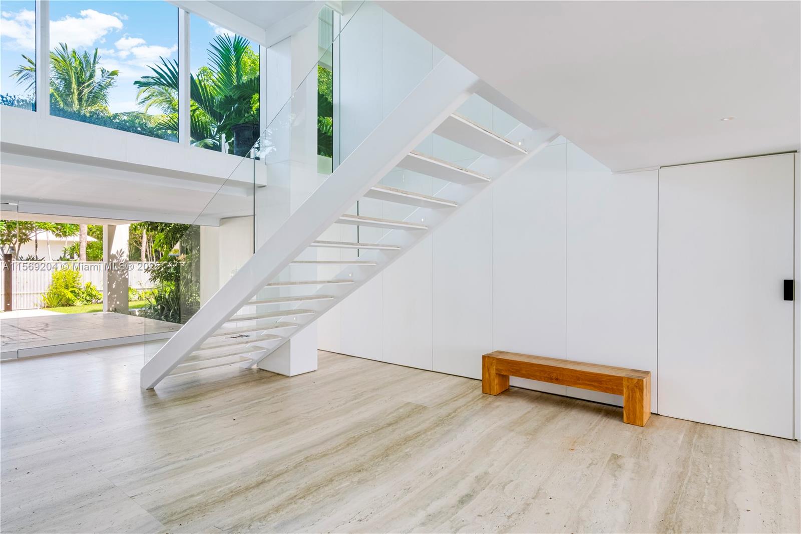 A modern, minimalist interior features a floating white staircase, stone flooring, and large glass windows — 440 S Mashta Dr, Key Biscayne FL 33149, KEY BISCAYNE, FL