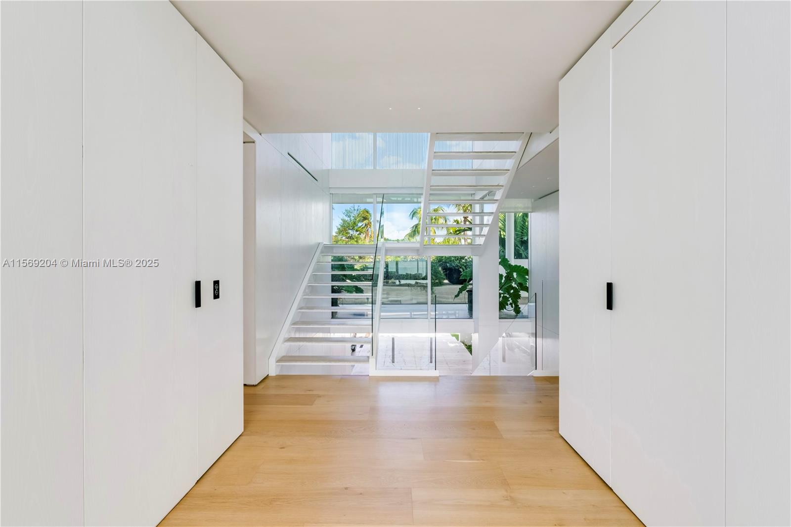 A minimalist entryway features white walls, light wood flooring, and a modern floating staircase — 440 S Mashta Dr, Key Biscayne FL 33149, KEY BISCAYNE, FL
