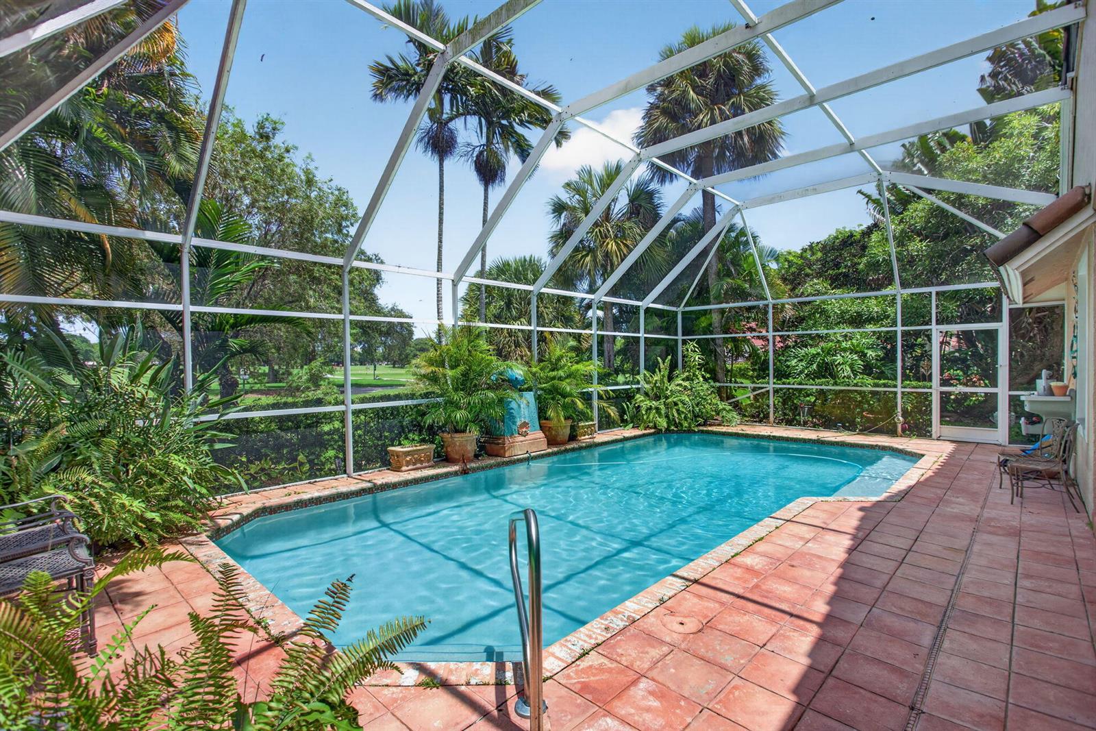 A screened-in swimming pool with a tiled deck surrounded by lush tropical landscaping and trees — 526 Misty Oaks Drive, Pompano Beach FL 33069, POMPANO BEACH, FL