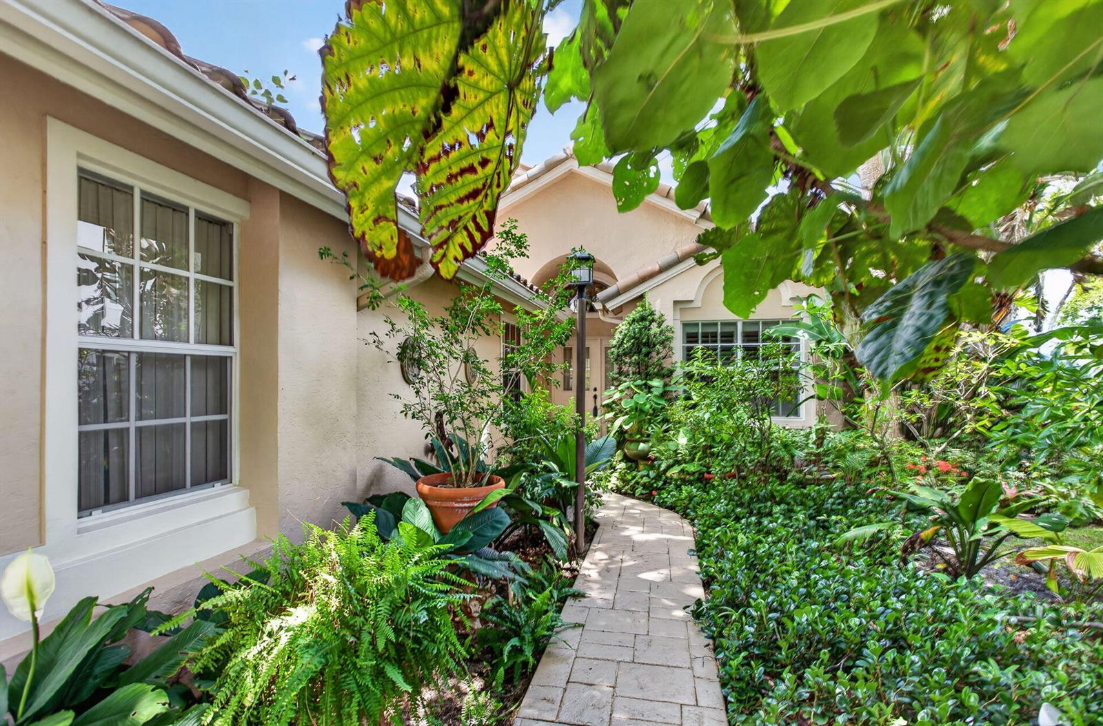 A stone walkway leads through lush landscaping to the entrance of a tan stucco house — 526 Misty Oaks Drive, Pompano Beach FL 33069, POMPANO BEACH, FL