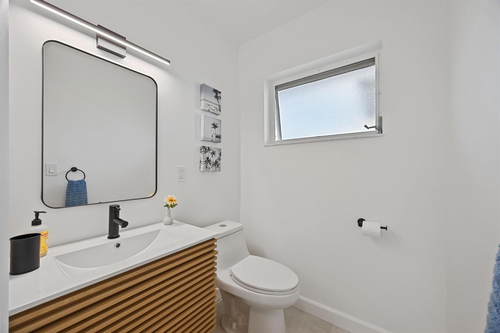 A modern bathroom features a slatted wood vanity, a black-framed mirror, and a white toilet — 2691 Dudley Dr Drive E # D, West Palm Beach FL 33415, WEST PALM BEACH, FL
