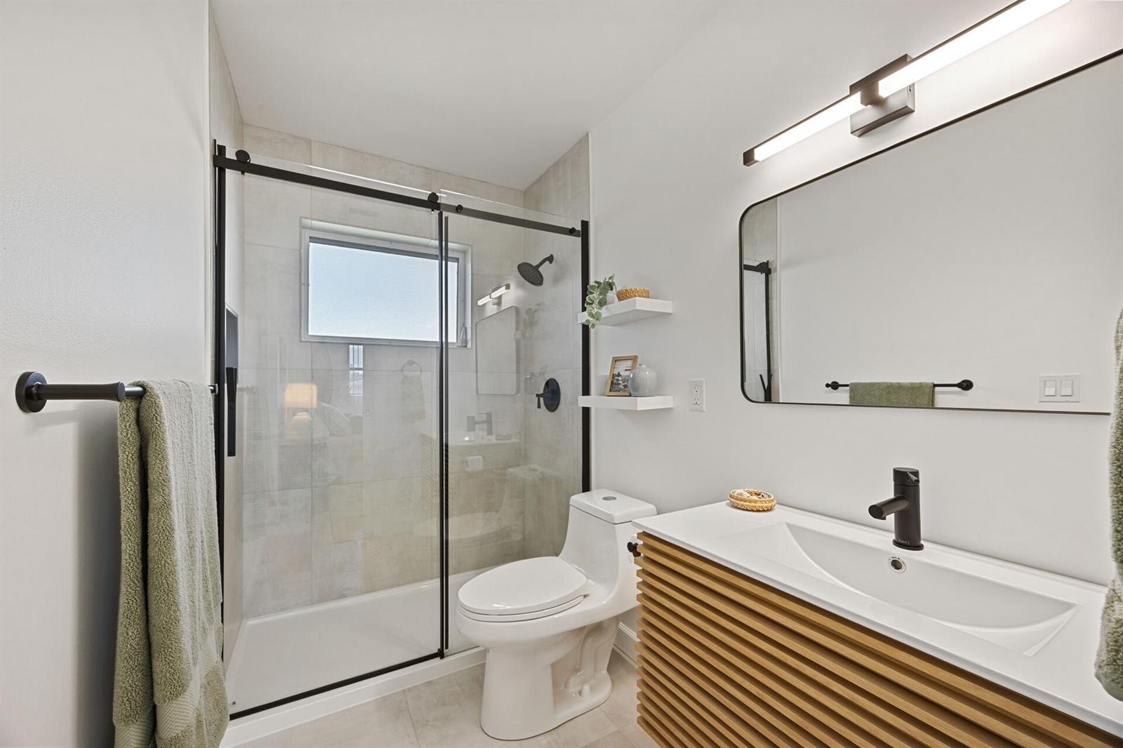 A modern bathroom features a glass-enclosed shower, a white toilet, and a slatted wood vanity — 2691 Dudley Dr Drive E # D, West Palm Beach FL 33415, WEST PALM BEACH, FL