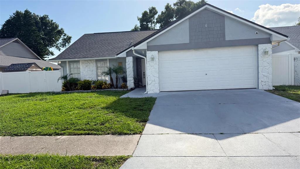 A single-story house features a white garage, stone accents, and a gray shingled roof — 7102 HOLLOWELL DRIVE, TAMPA, FL