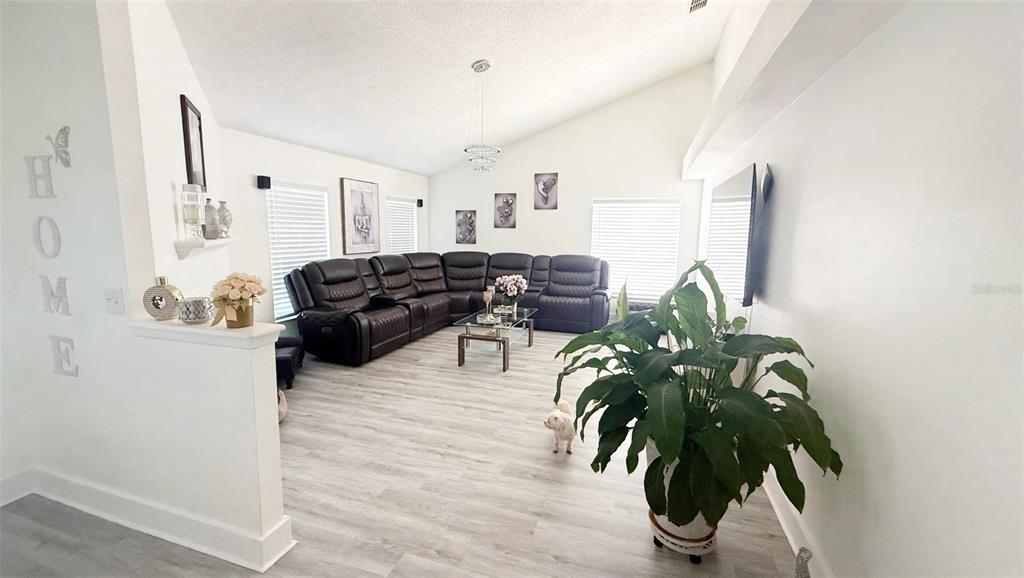 A living room features light wood-look flooring, a large sectional sofa, and a vaulted ceiling — 7102 HOLLOWELL DRIVE, TAMPA, FL