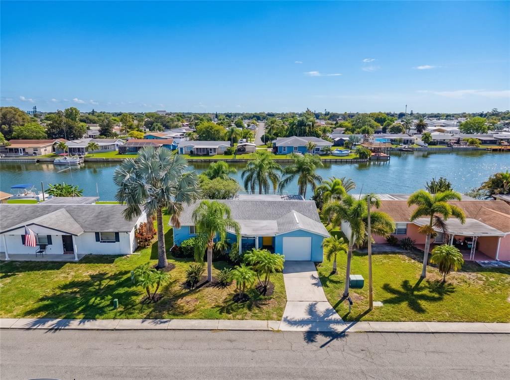 An aerial view shows a blue house with a driveway and palm trees by water — 2228 SOCIETY DRIVE, HOLIDAY, FL