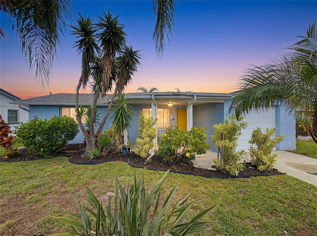 A blue single-story house with a yellow front door and tropical landscaping at sunset — 2228 SOCIETY DRIVE, HOLIDAY, FL