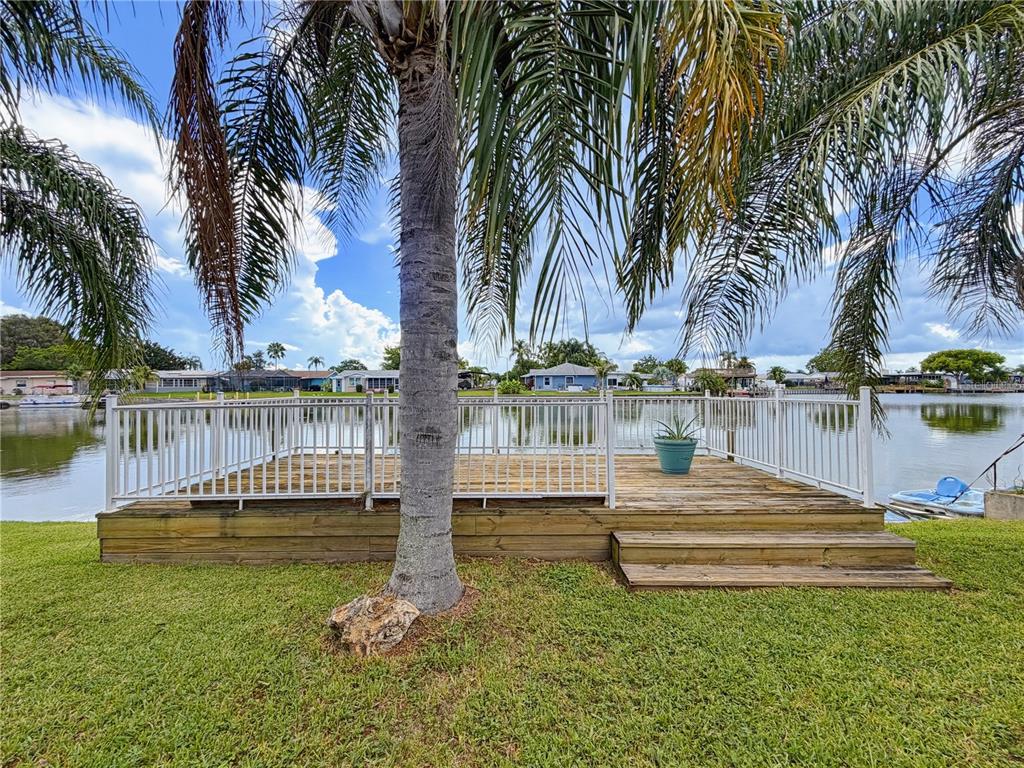 A wooden deck with white railings overlooks a lake under a palm tree — 2228 SOCIETY DRIVE, HOLIDAY, FL