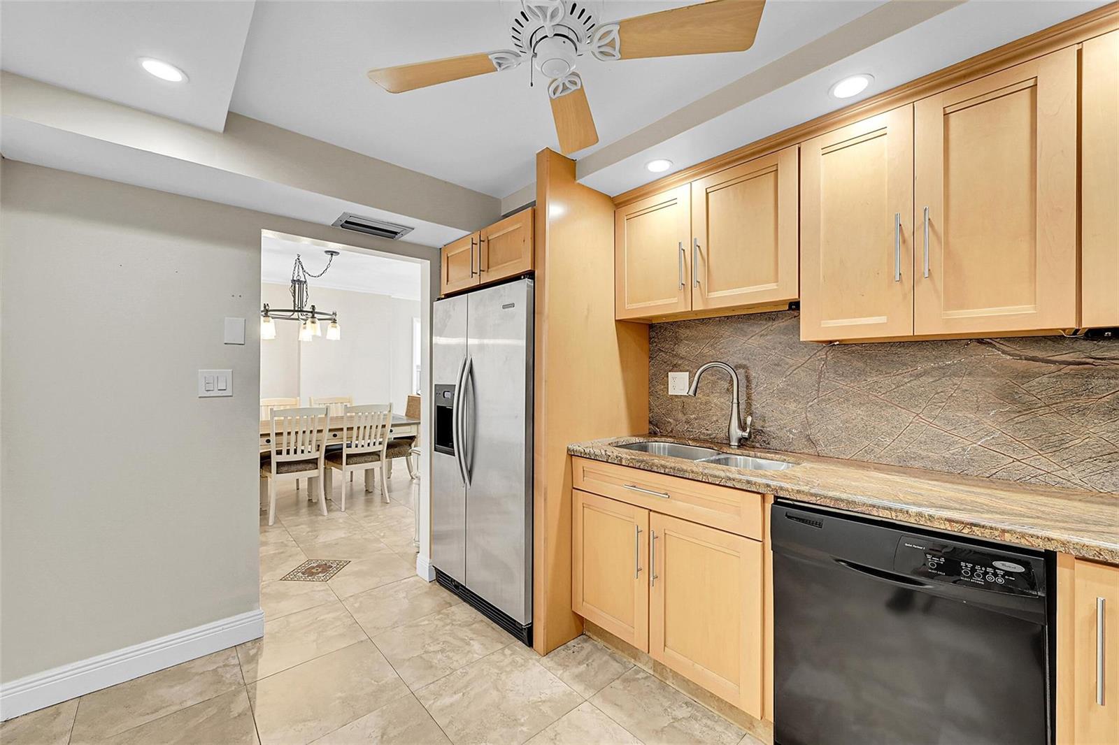 A kitchen features light wood cabinets, stainless steel appliances, a stone backsplash, and tile flooring — 525 N Ocean Boulevard # 919, Pompano Beach FL 33062, POMPANO BEACH, FL
