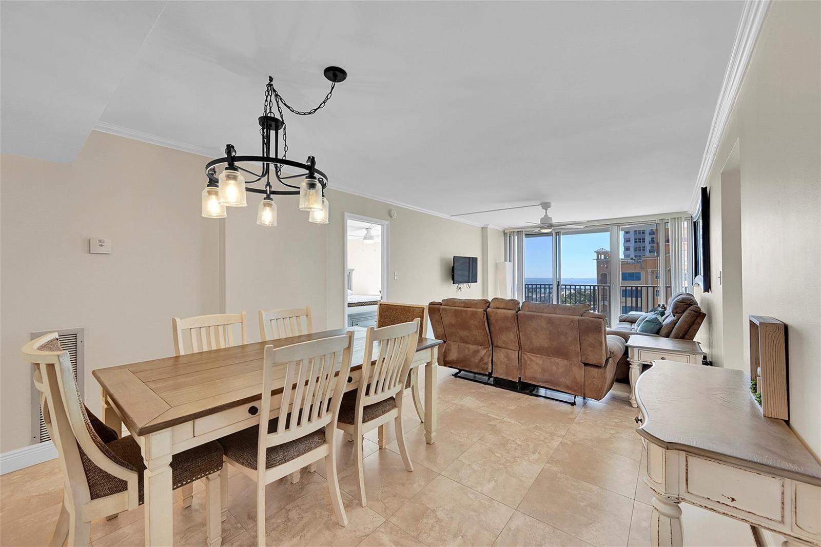 A dining area with a wooden table and chandelier opens to a living room with ocean views — 525 N Ocean Boulevard # 919, Pompano Beach FL 33062, POMPANO BEACH, FL